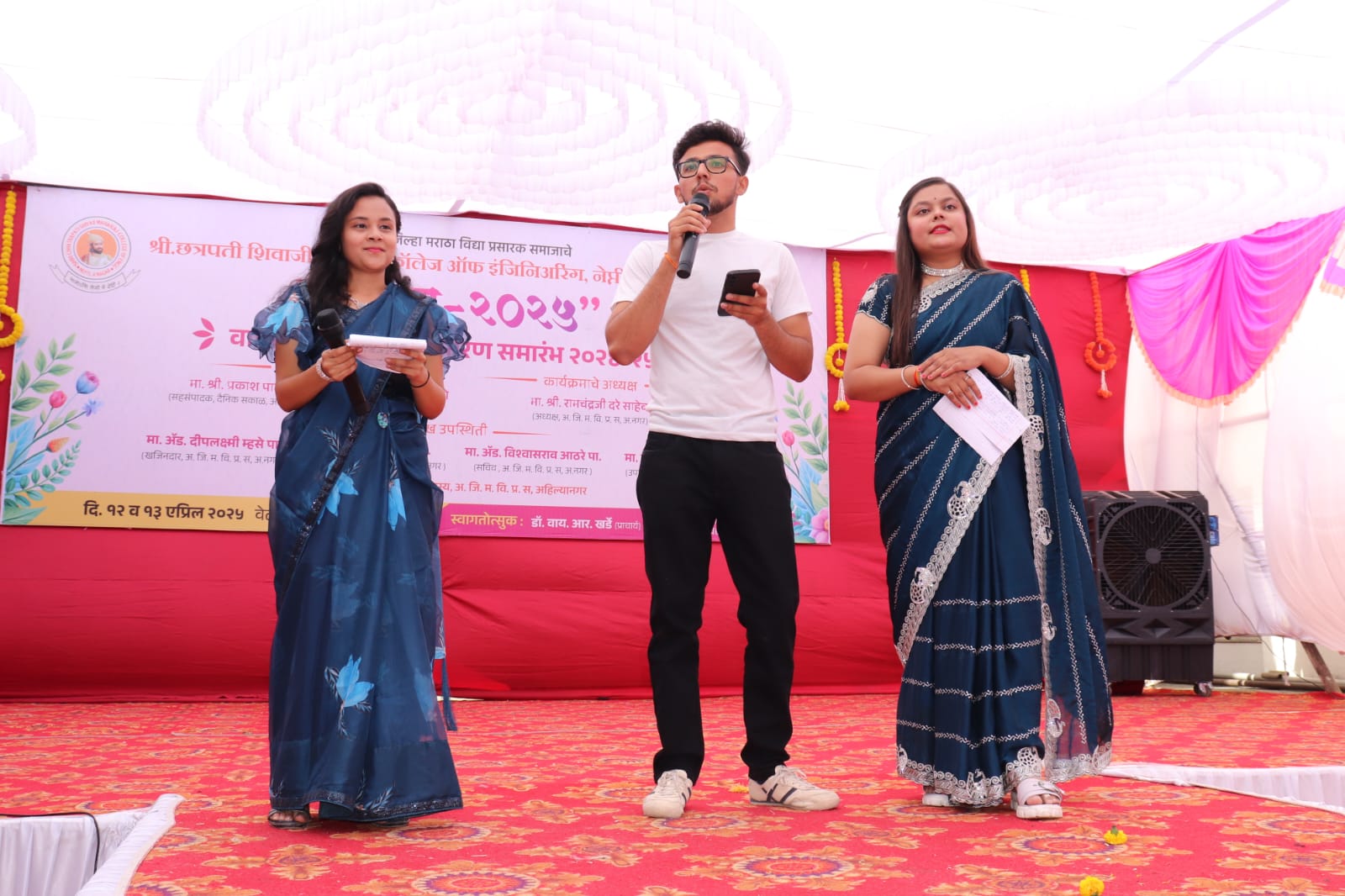 Onkar Kandekar hosting a college event on stage with a microphone alongside two co-hosts