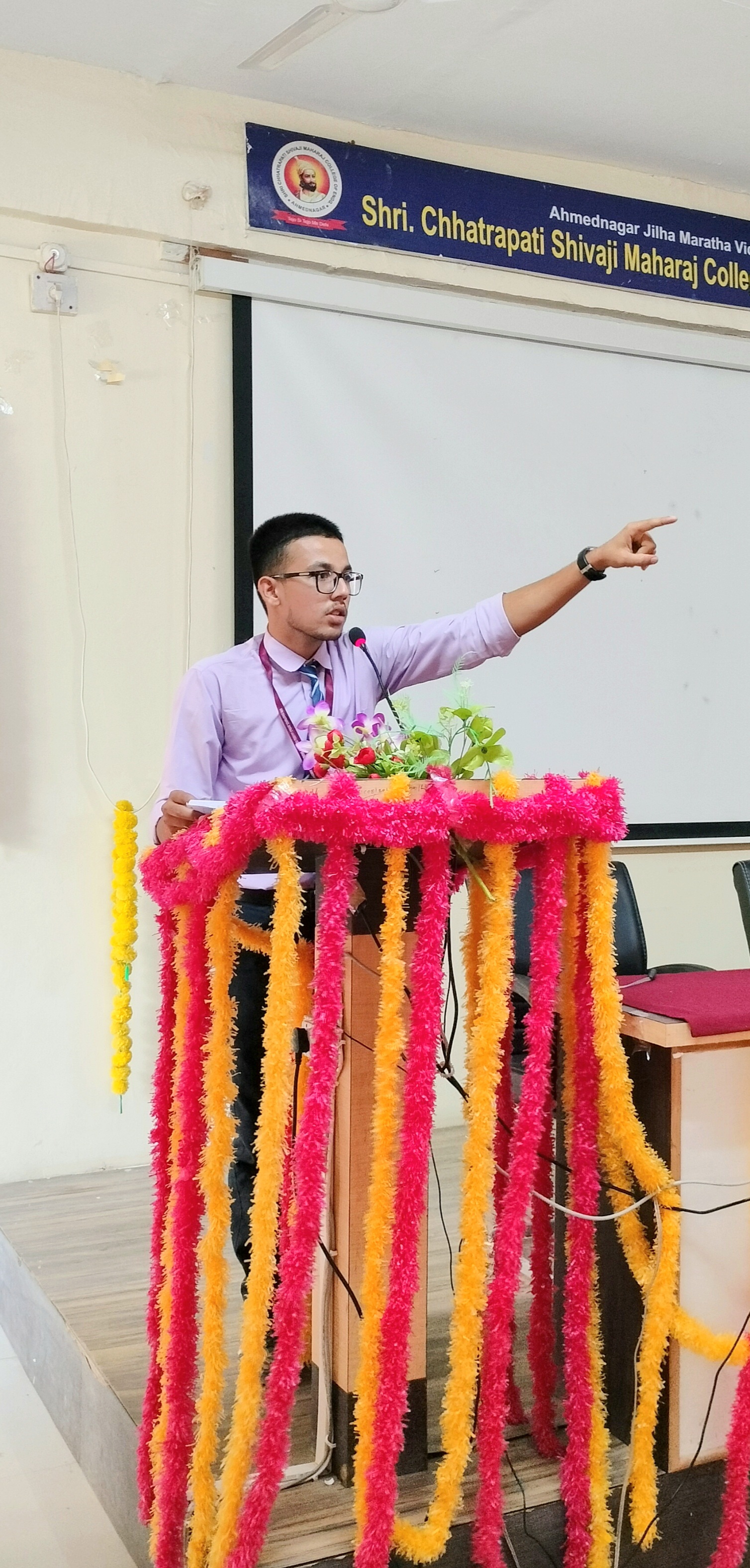 Onkar Kandekar addressing an audience from a decorated podium in a college seminar hall